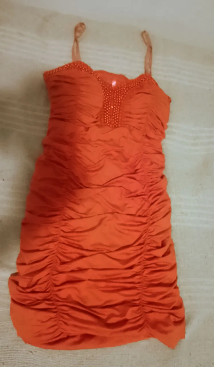 Vestido corto naranja con tiras finas y detalles de perlas en el escote. Posee fruncidos en toda la prenda.