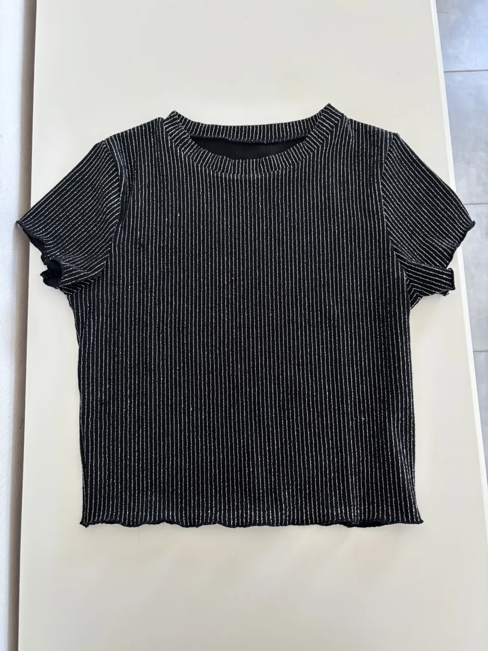 Remera negra con finas rayas verticales plateadas. Escote redondo y mangas cortas.