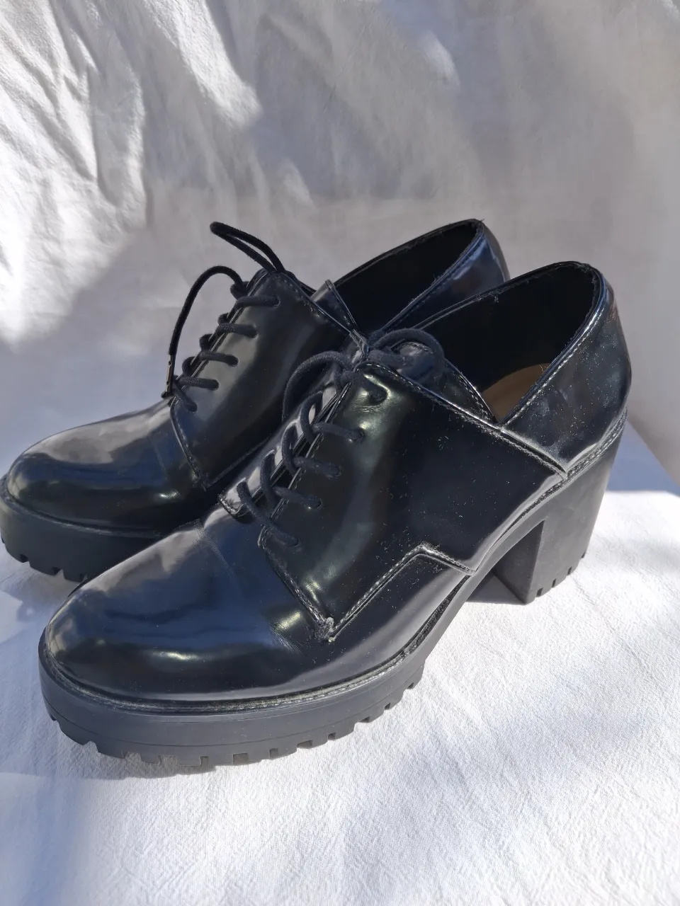 Zapatos negros de charol con cordones y plataforma gruesa. Tienen taco alto y diseño tipo Oxford.