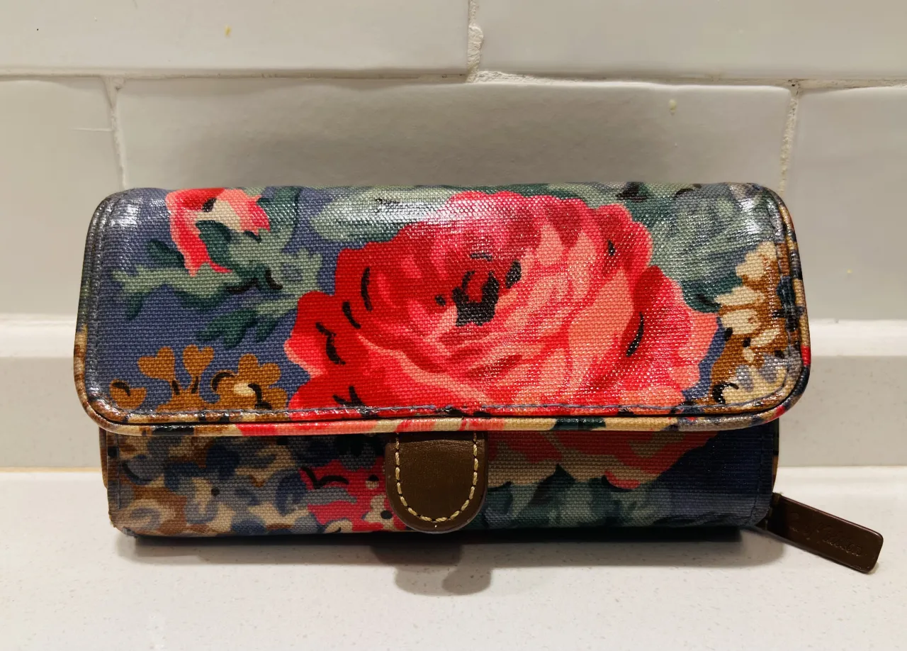 Billetera con estampa floral de rosas rojas y flores pequeñas sobre fondo azul. Posee cierre y broche.plastificada
original Cath Kitson 