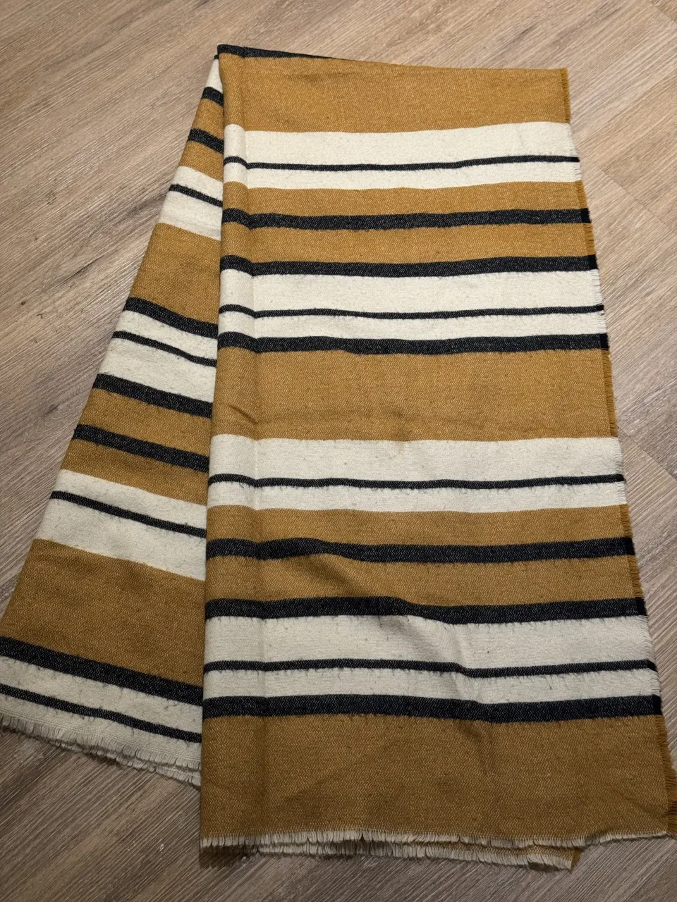 Bufanda a rayas horizontales en tonos ocre, blanco y negro. Posee flecos en los extremos. Tiene manchitas, no se ven casi  al usarla pero si la extendes tipo manta si. 