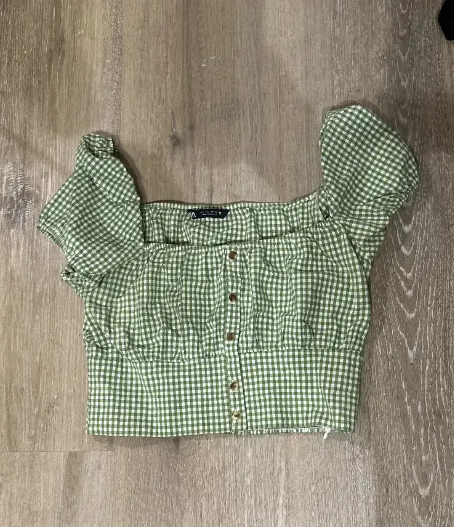 Blusa crop con estampado de cuadros vichy en verde y blanco. Diseño con mangas abullonadas y botones delanteros. Ideal para un look fresco y casual.