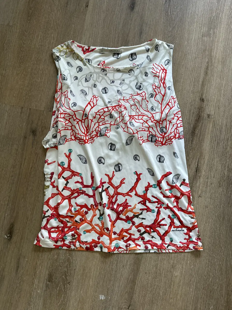 Musculosa de mujer con estampado de motivos marinos, ideal para el verano. Confeccionada en poliéster y elastano, ofrece comodidad y ajuste. Diseño con coral y conchas marinas.