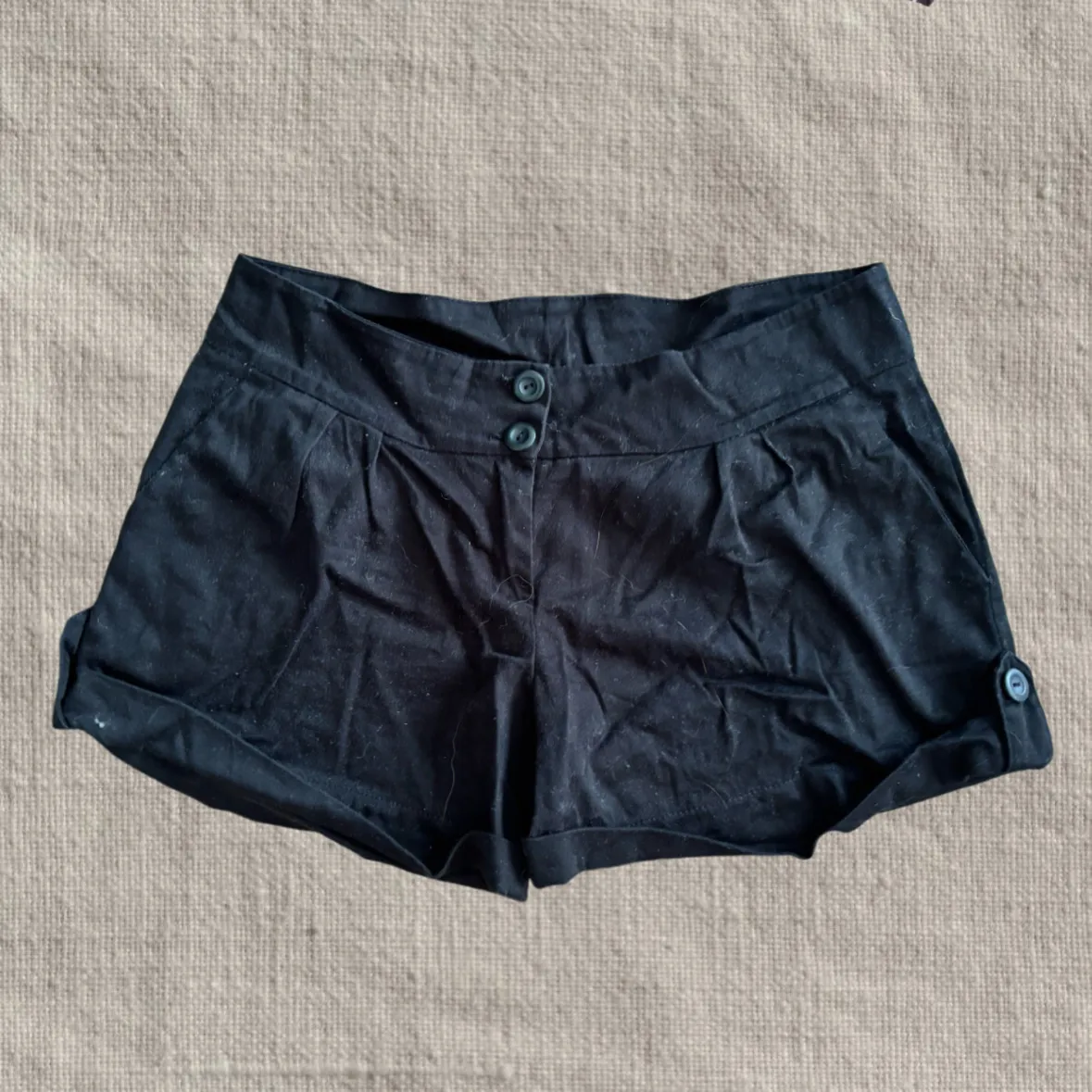 Shorts negros con dos botones en la cintura y detalle de pinzas. Posee doblez en los bordes inferiores de las piernas y un botón decorativo en cada lateral.