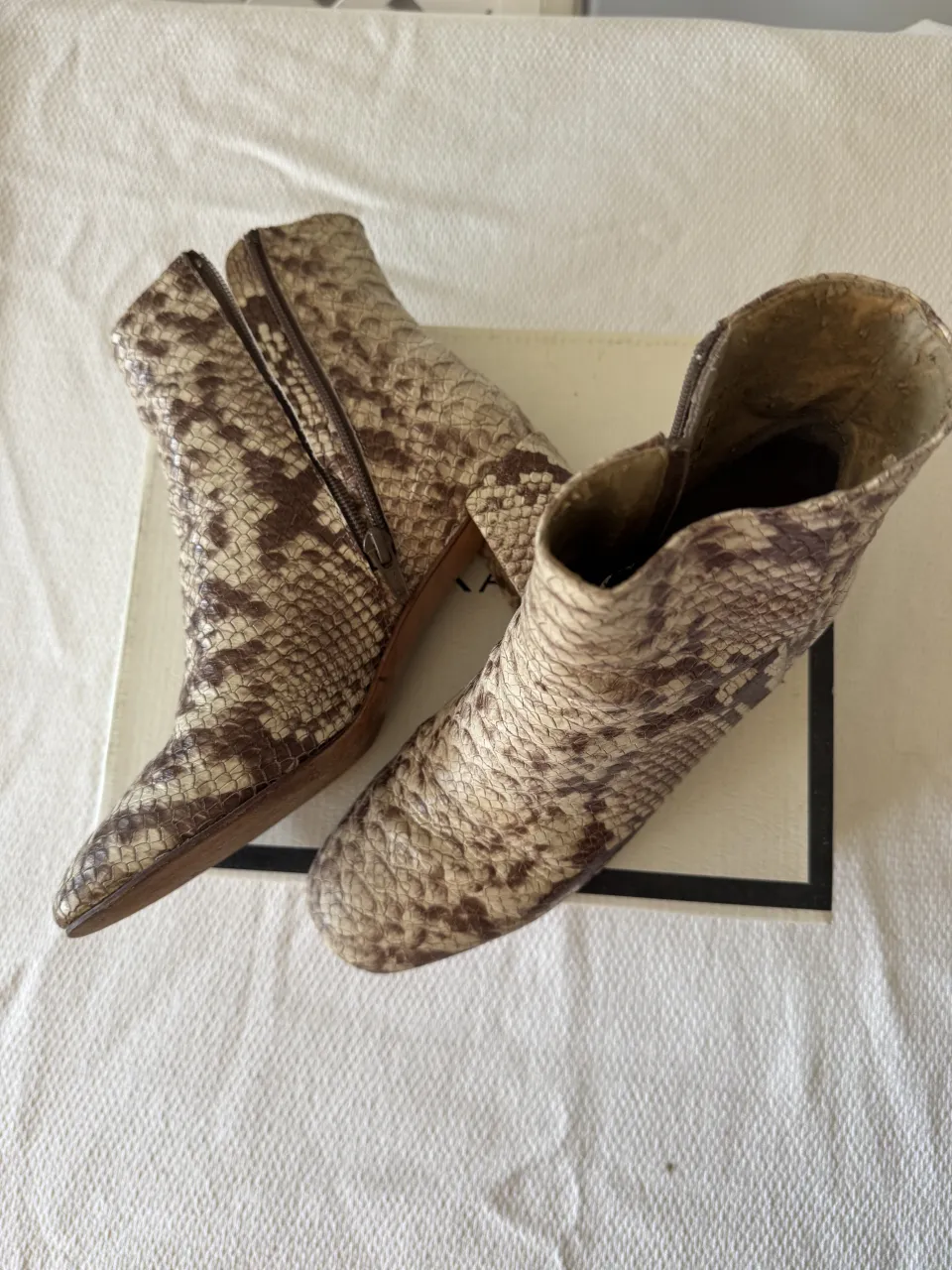 Botas de cuero con estampado de serpiente en tonos beige y marrón. Tienen cierre lateral y taco grueso.