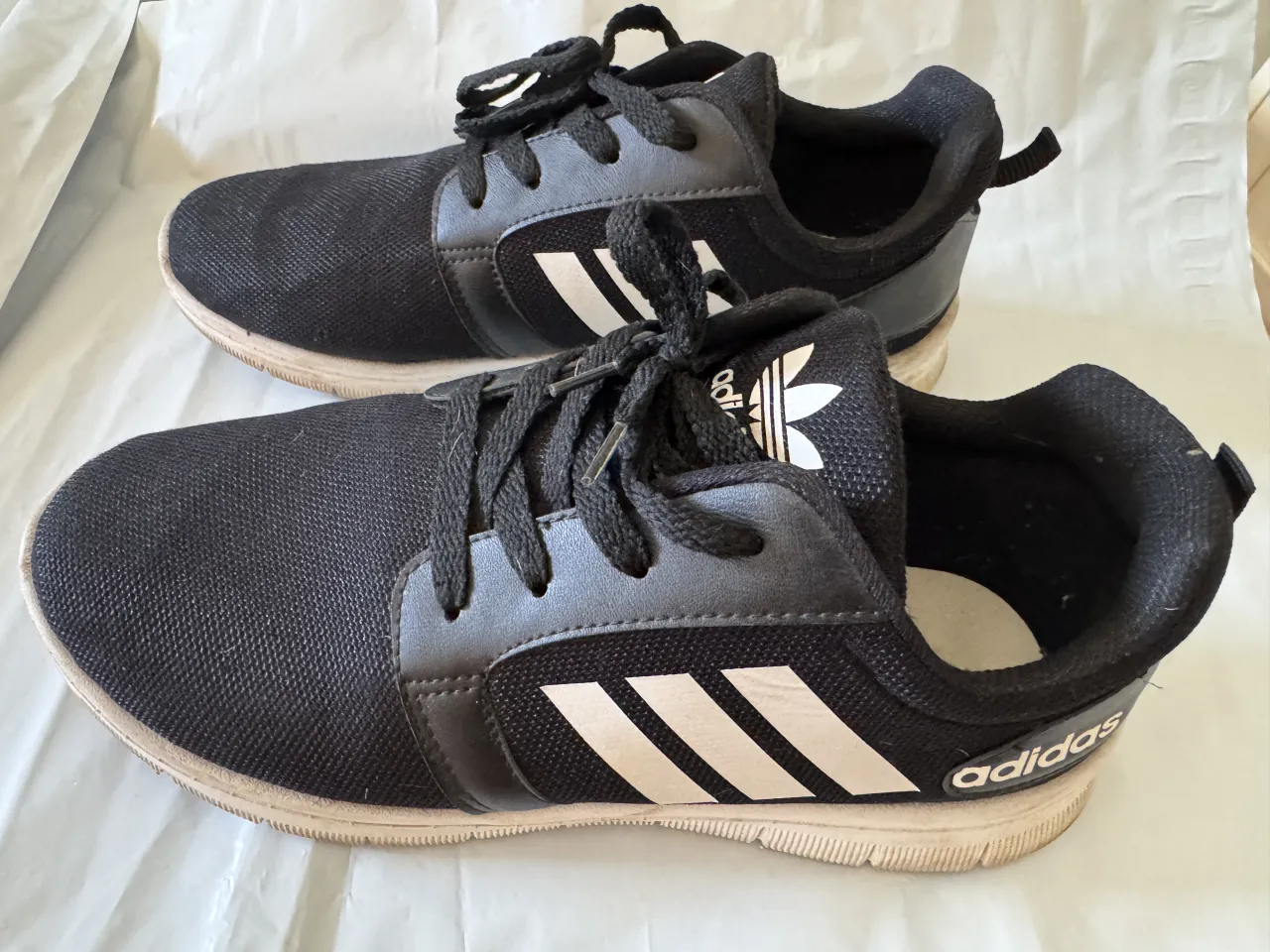 Zapatillas deportivas negras con detalles en blanco y suela desgastada.