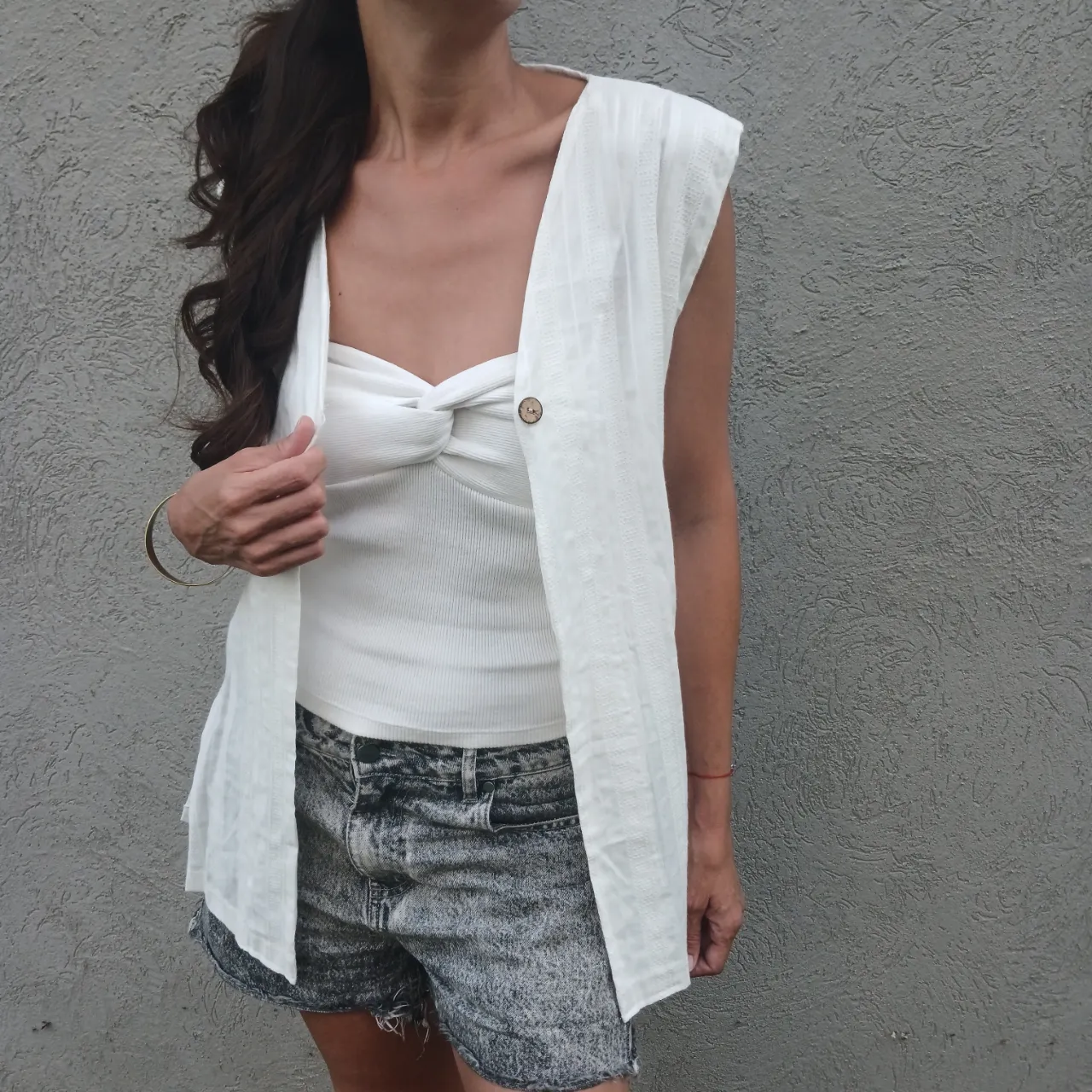 Chaleco blanco de tela liviana con botones de madera. Posee un diseño de líneas verticales finas y un bolsillo interno.