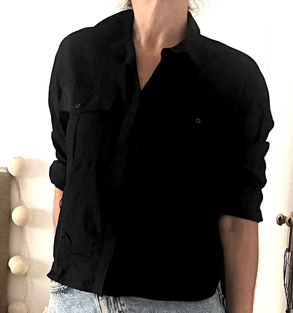 Camisa negra de manga larga con dos bolsillos en el frente y cordones laterales para ajustar. Se puede usar con mangas arremangadas.