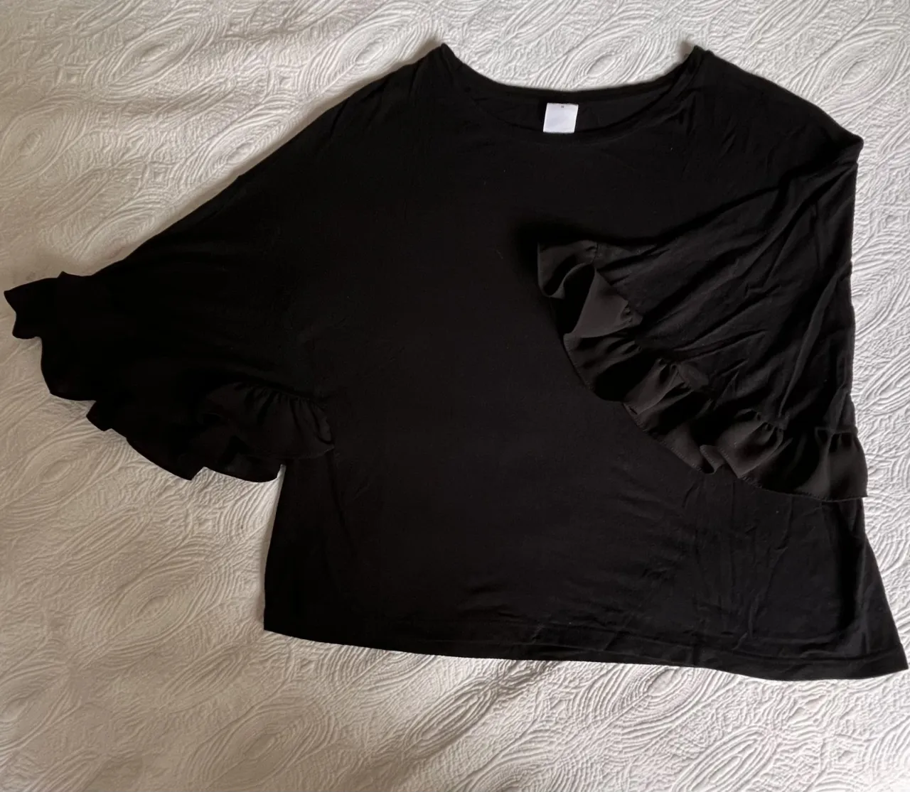 Remera negra de manga corta con volados en los puños.