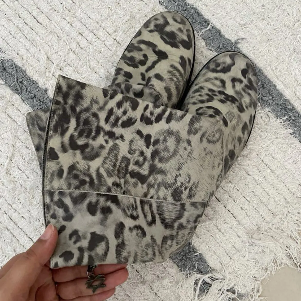 Botas de caña media con estampa animal print en tonos grises y negros. Tienen un detalle metálico en la parte superior de la caña.