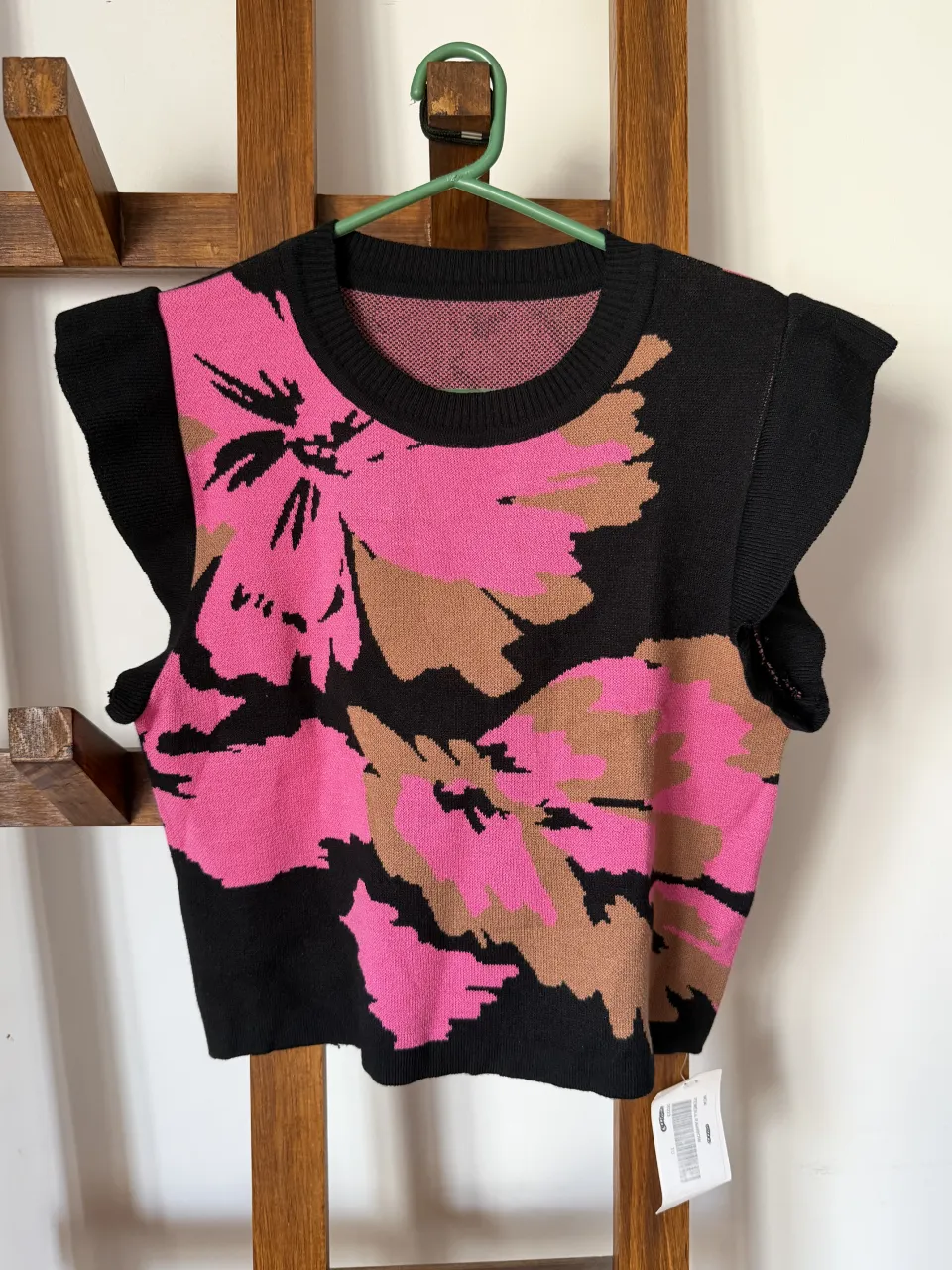 Top tejido sin mangas con estampa floral vibrante en tonos fucsia y marrón sobre fondo negro. Diseño moderno y canchero, ideal para combinar con jeans o faldas.