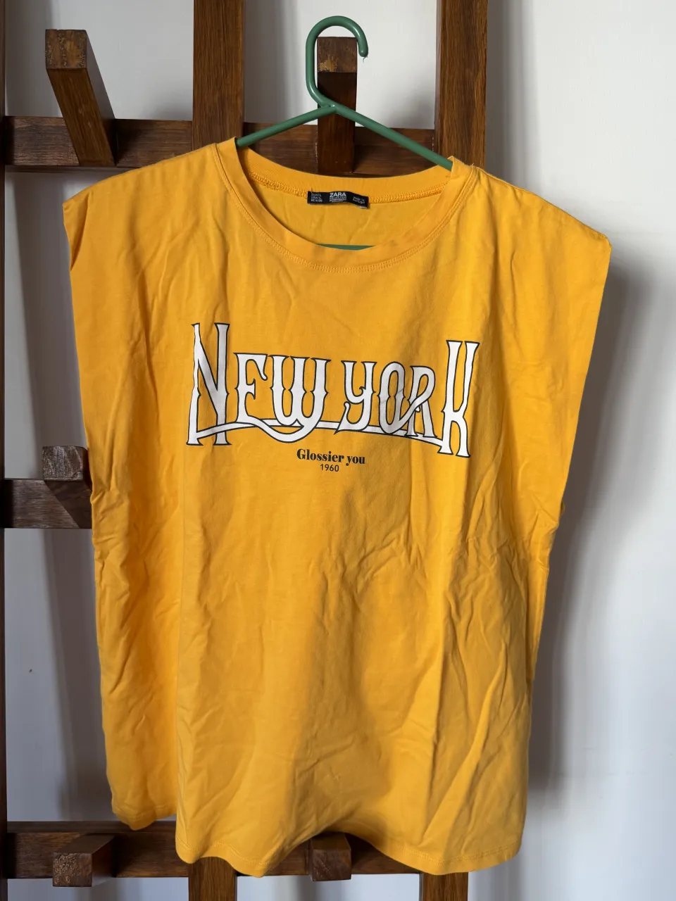 Remera amarilla sin mangas con estampa "New York" y "Glossier you 1960". Ideal para un look casual y urbano.