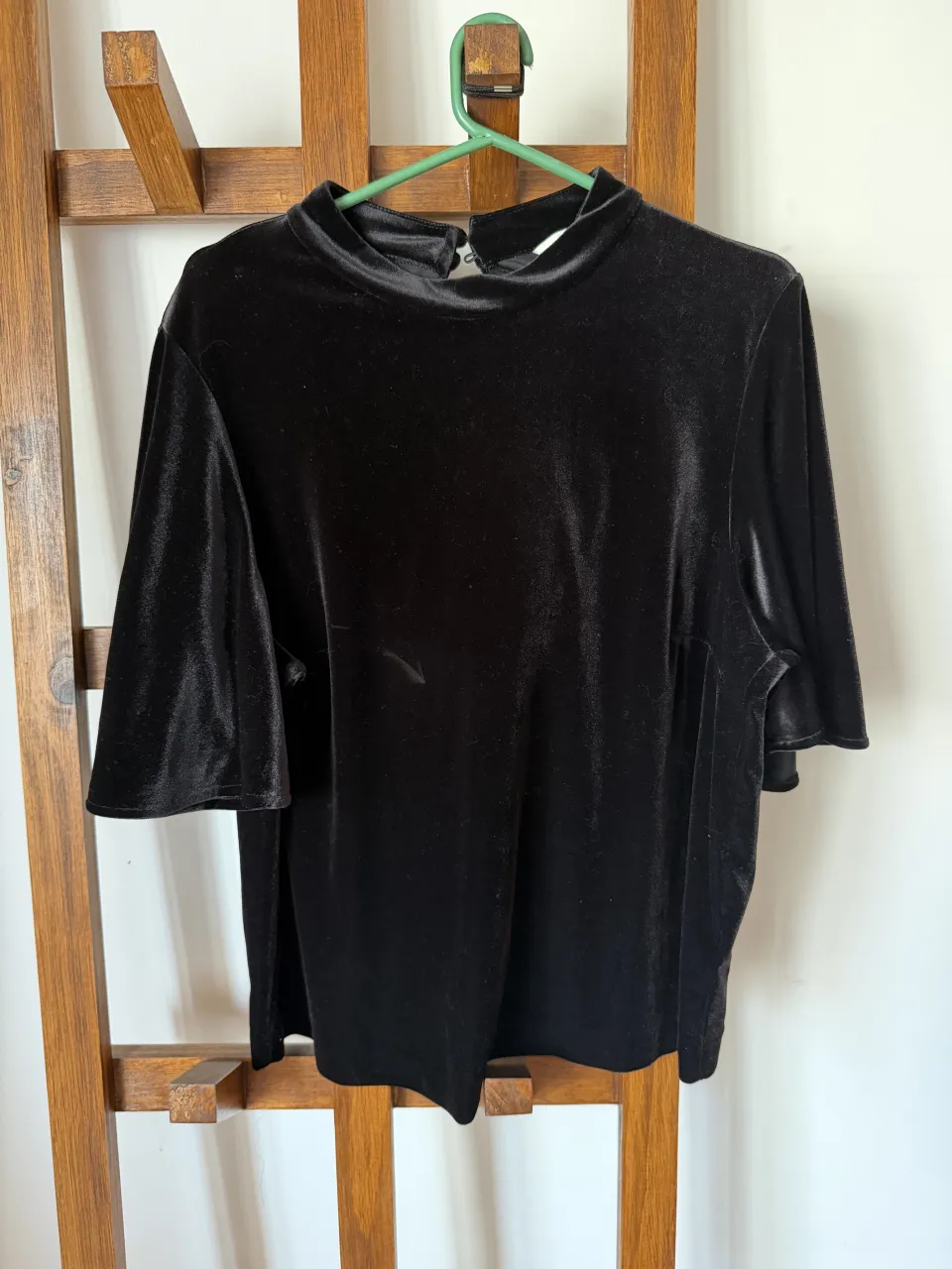 Remera negra de terciopelo con cuello alto y mangas cortas acampanadas. Posee un detalle de recorte circular en la espalda con dos botones forrados para cerrar. Ideal para un look elegante y sofisticado. Detalle: mancha - ver foto