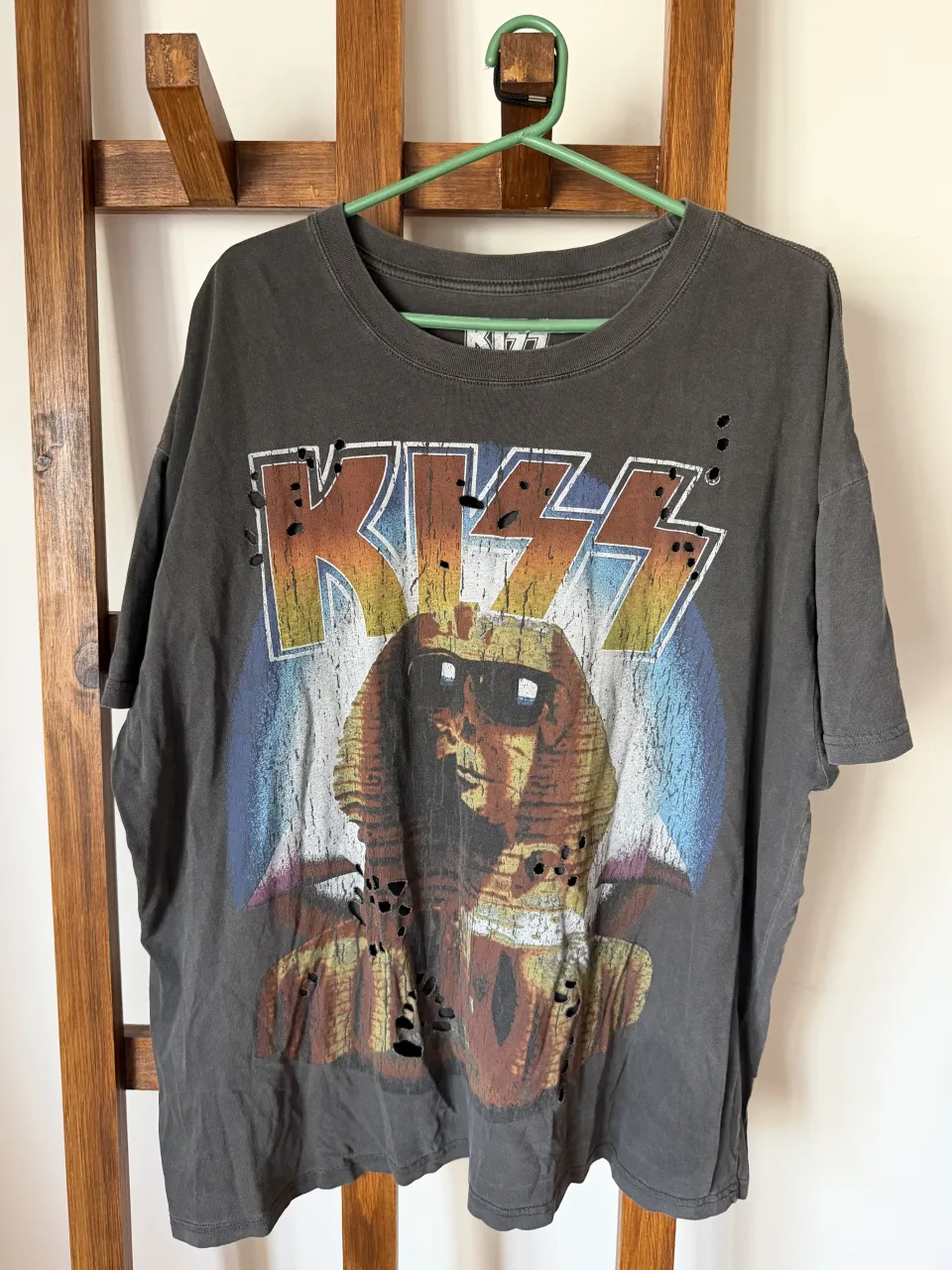 Remera oversize gris oscuro con estampa "KISS" y diseño de esfinge con anteojos. Tiene detalles de roturas y desgaste que le dan un toque rocker y vintage. Ideal para un look casual y canchero.