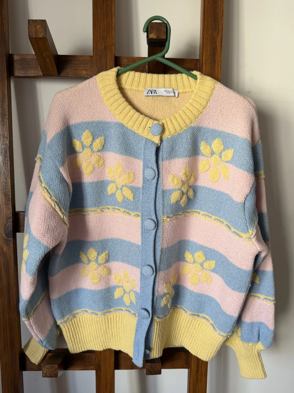 Cardigan de tejido suave con rayas horizontales en rosa, celeste y amarillo. Posee apliques de flores amarillas en relieve y detalles de costura a tono. Puños y cintura elastizados.