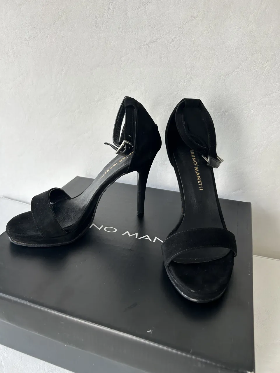 Sandalias negras de taco alto con tiras finas y hebilla para ajustar en el tobillo. Marca Bruno Manetti.