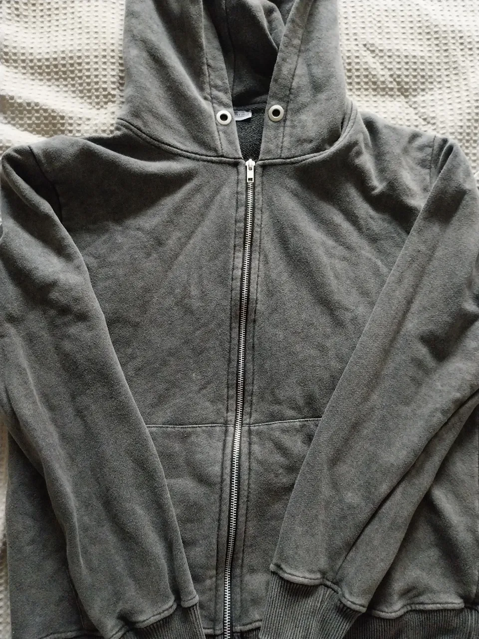 Buzo gris con capucha y cierre completo. Posee bolsillos frontales tipo canguro.