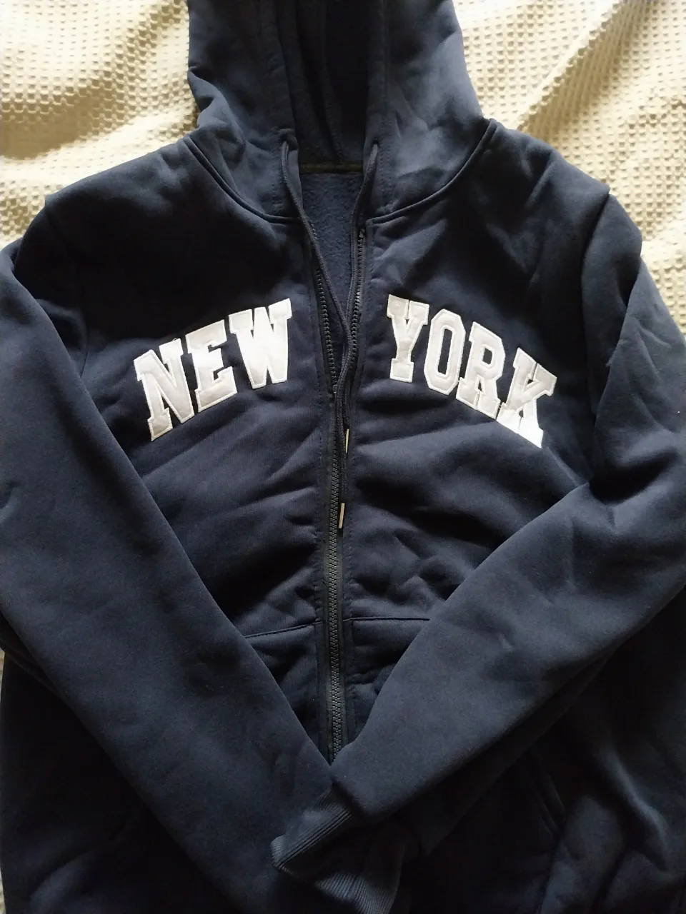 Buzo azul marino con capucha y cierre completo. Estampado blanco con la inscripción "NEW YORK" en el frente.