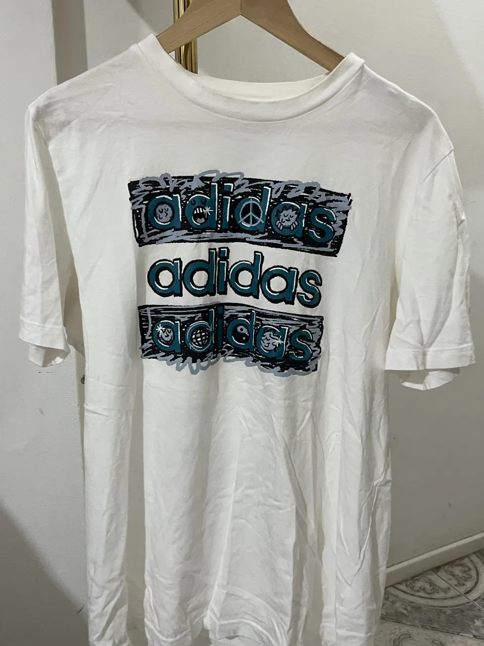 Remera blanca de manga corta con estampa de Adidas en el frente. Ideal para un look casual y deportivo.