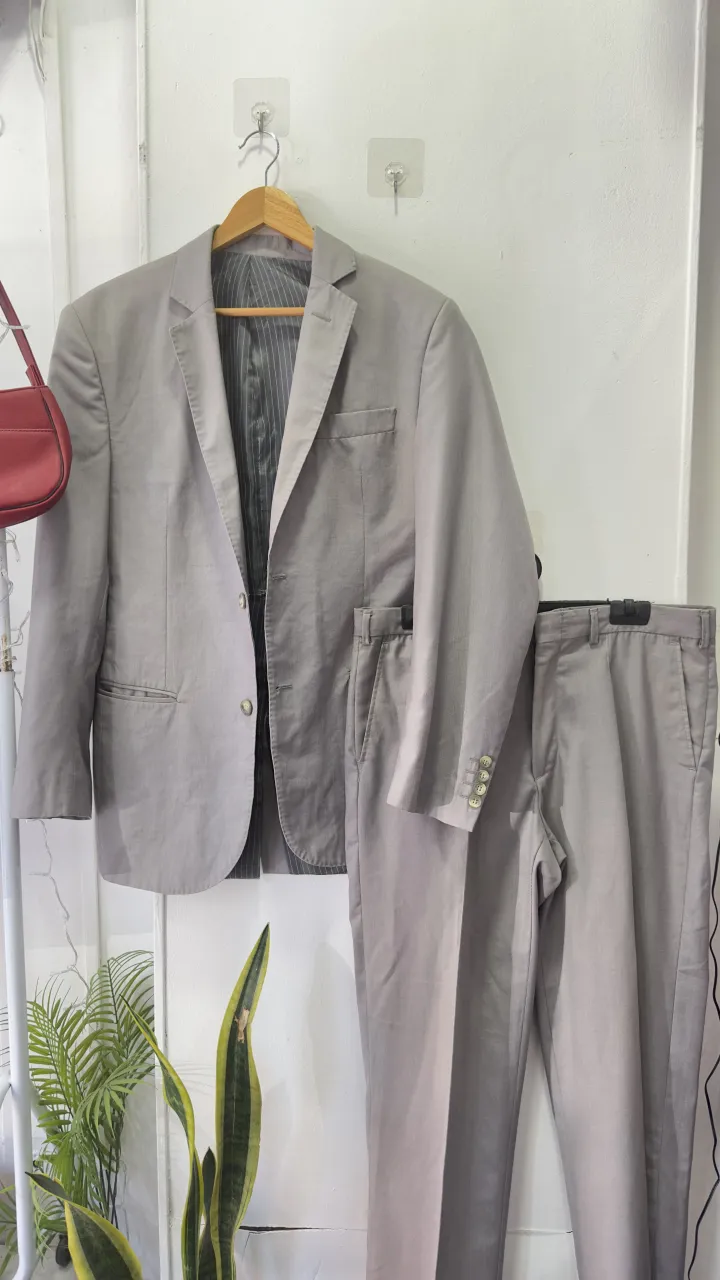 Traje de vestir gris de dos piezas, ideal para eventos formales o para un look de trabajo elegante. El saco tiene un corte clásico con solapa y un bolsillo en el pecho. El pantalón a juego completa el conjunto.
