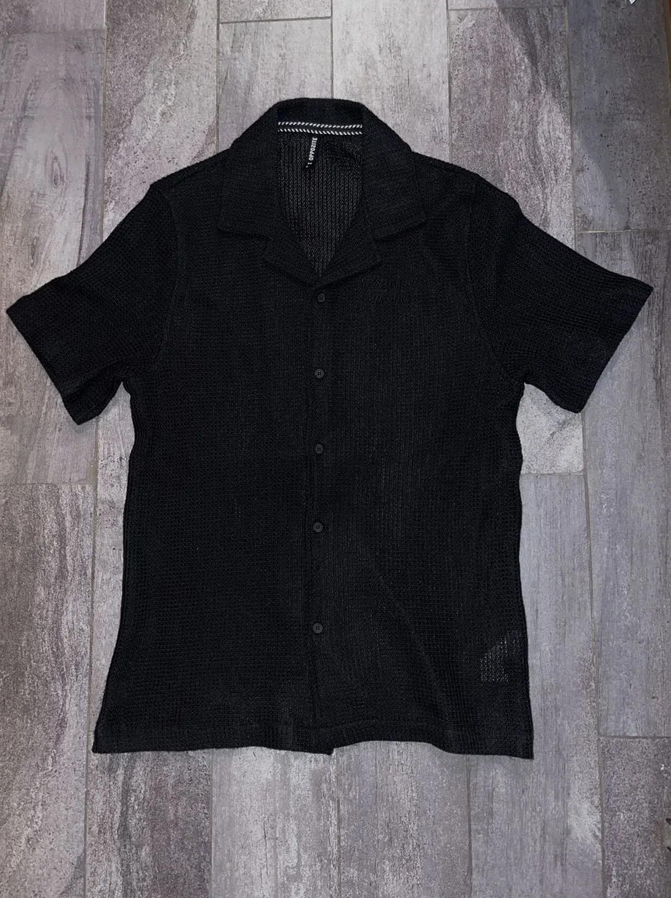 Camisa negra de manga corta con cuello solapa y botones al frente. Posee un bordado en la espalda con la palabra "Focus" se ve blanco por el flash. Comprada en Chile. Lavar a mano con agua fria, tiene una textura panal