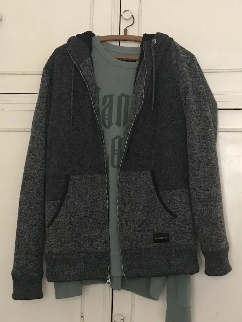 Buzo con cierre Quiksilver para hombre, de color gris y negro, con capucha y bolsillos. Ideal para el invierno. Por dentro es de corderito.