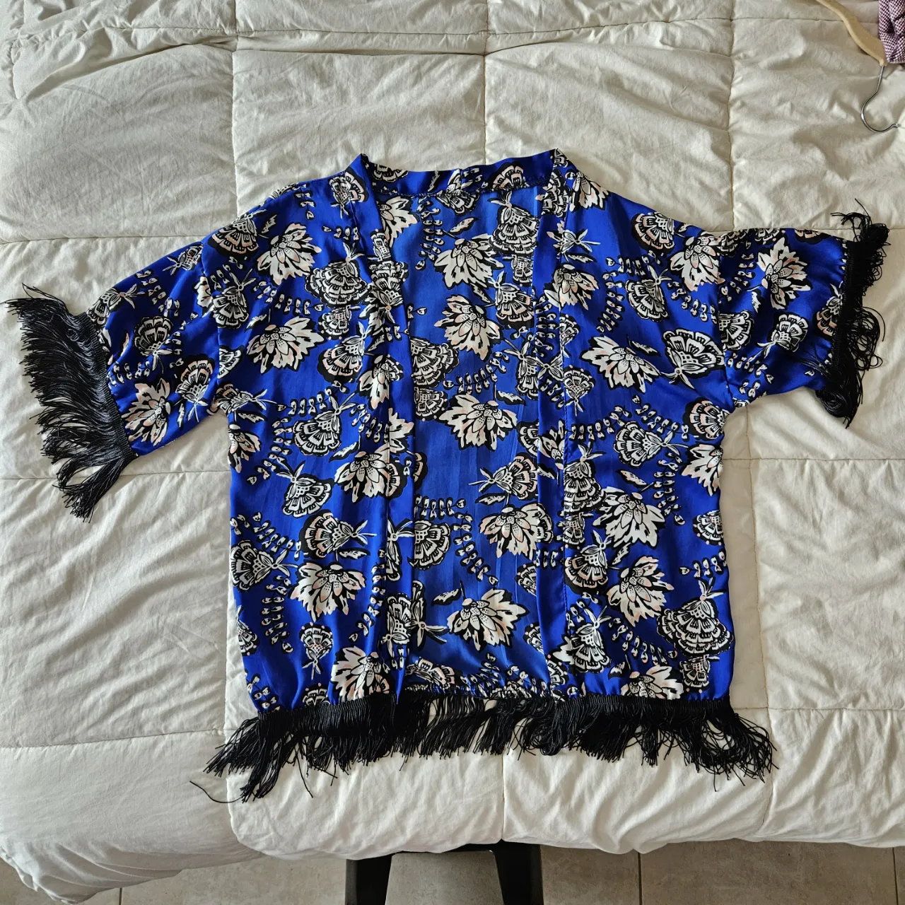 Kimono súper fresco y liviano con un estampado floral vibrante en azul eléctrico. Tiene mangas cortas y un detalle de flecos negros en puños y ruedo que le dan un toque bohemio y chic. Ideal para usar abierto sobre un top o vestido, perfecto para un look de verano o para darle un toque especial a cualquier outfit.