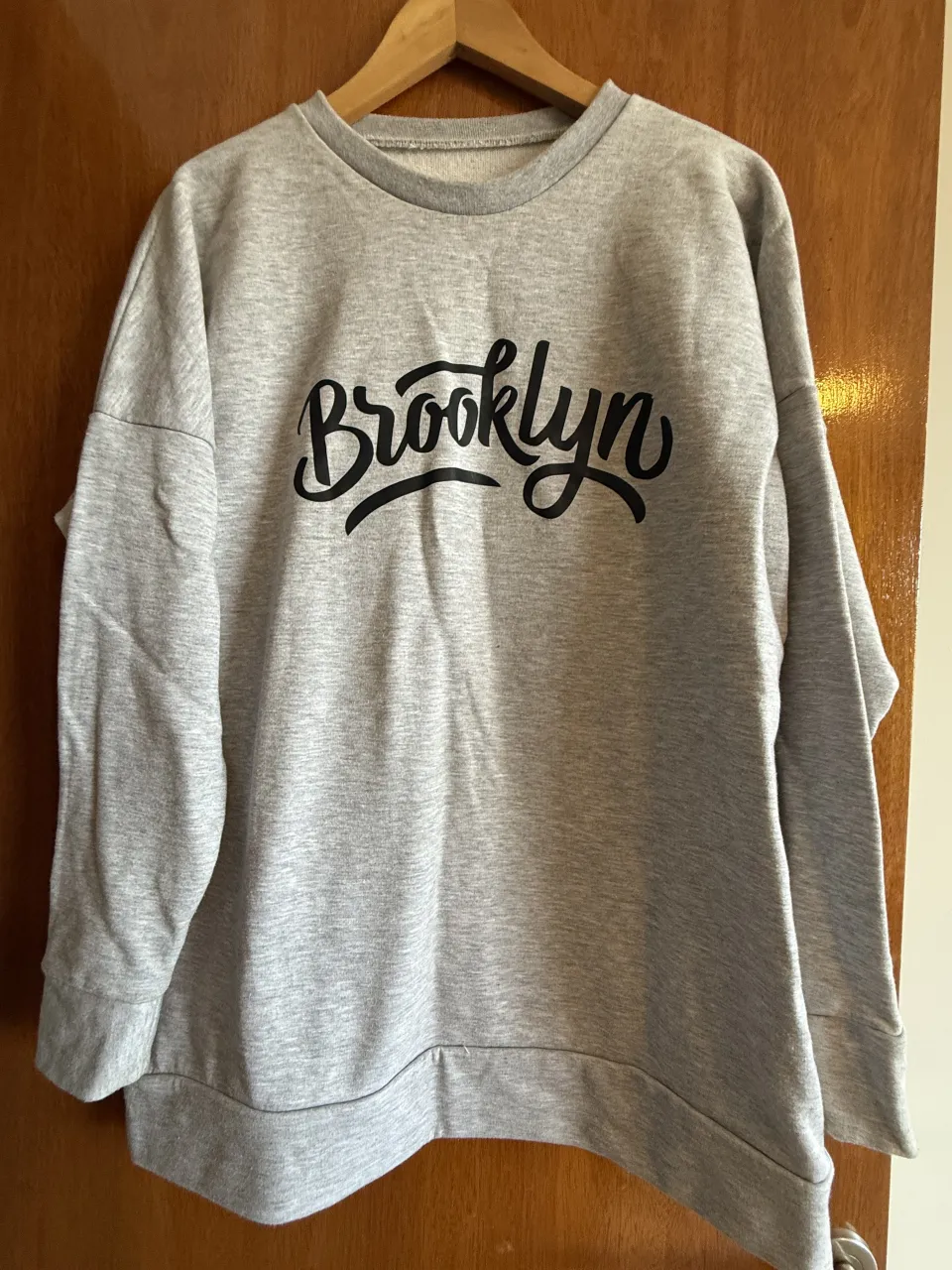 Buzo gris con estampa "Brooklyn" en negro. Cuello redondo y mangas largas.