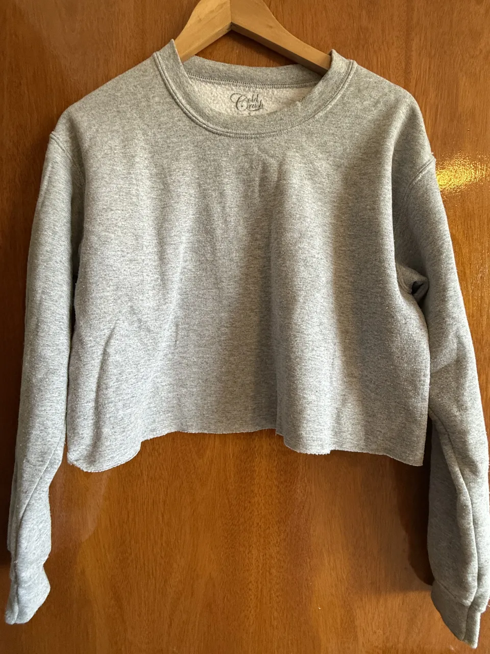 Buzo crop gris con mangas largas y cuello redondo. Posee un corte deshilachado en la parte inferior.