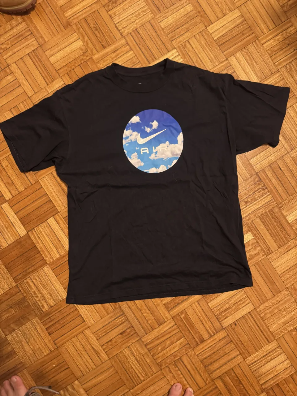 Remera negra de algodón con estampa circular de cielo y nubes con el logo de Nike y la palabra "AIR". Ideal para un look casual y deportivo.