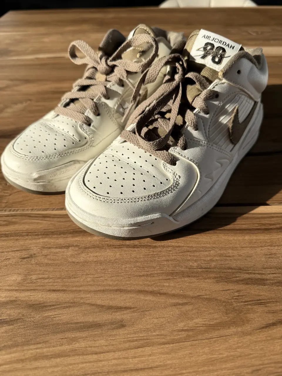 Zapatillas Air Jordan 98 blancas con detalles en marrón verdoso. Tienen cordones y el logo de Nike en la parte trasera. Ideales para un look casual y urbano.