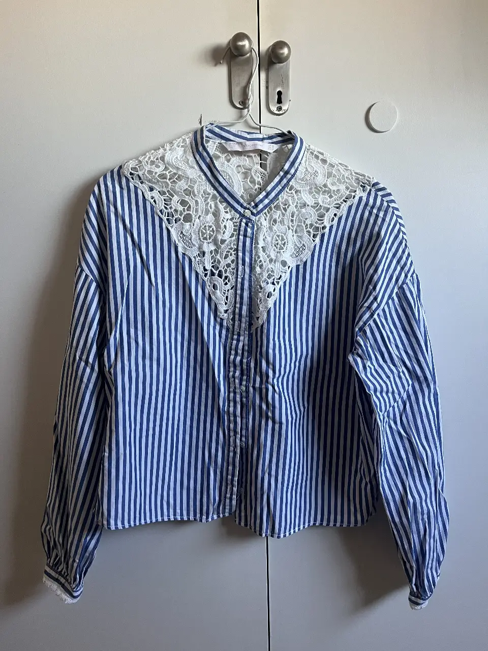 Blusa de mujer a rayas azules y blancas con detalle de encaje en el pecho. Manga larga con puños y cuello mao. Ideal para un look casual y elegante.