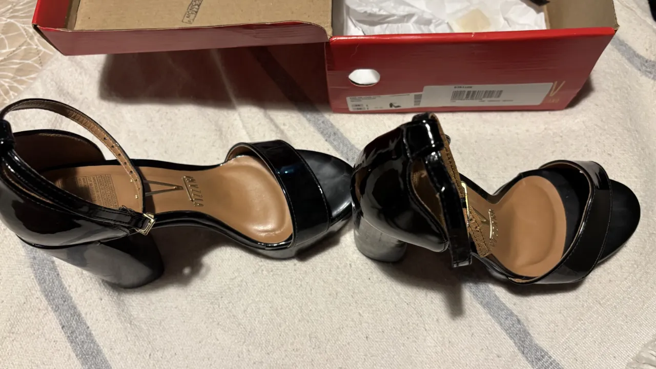 Sandalias negras de charol con taco alto y plataforma. Tienen una tira fina en el empeine y otra que rodea el tobillo con hebilla. Ideales para fiestas o eventos formales.