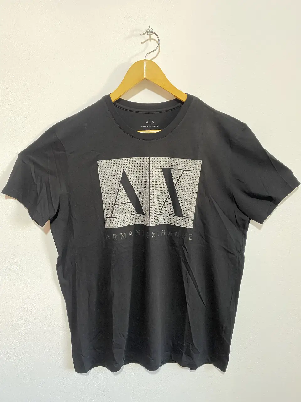 Remera Armani Exchange, negra de hombre, talle XL. Confeccionada en algodón, presenta un diseño con el logo de la marca estampado en la parte delantera con detalles de strass. Ideal para un look casual y moderno.