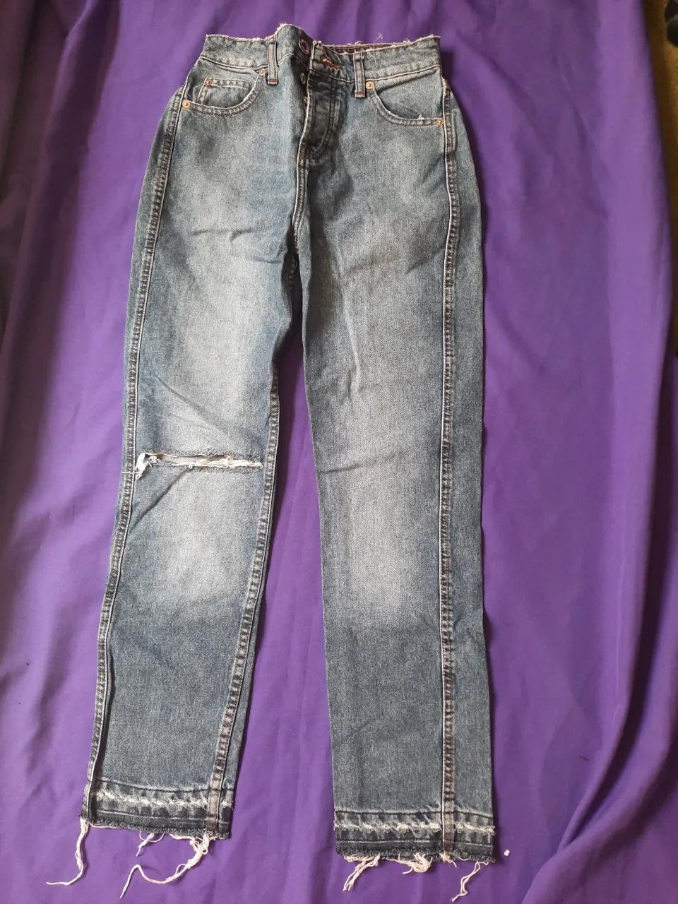 Jeans mom de denim con rotura en la rodilla derecha y detalles deshilachados en los bajos. Presentan costuras visibles. Talle 34 (Xs).