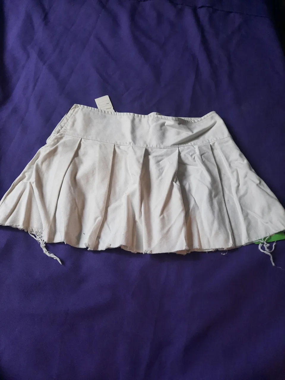 Pollera corta blanca con tablas y detalles deshilachados en el borde inferior. Tiro bajo.