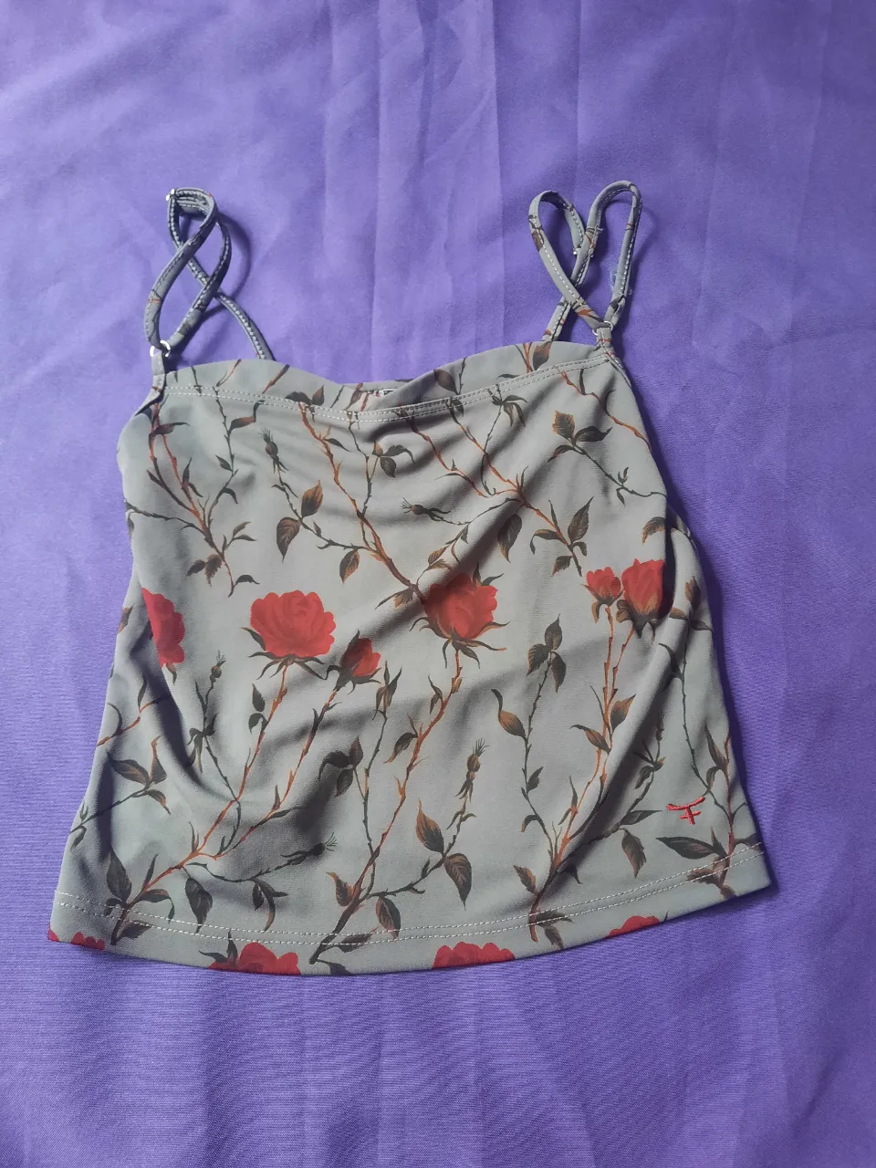 Top con breteles finos y estampa floral de rosas rojas y hojas verdes sobre fondo gris. Posee un detalle de corazón con las iniciales KSK en la etiqueta.