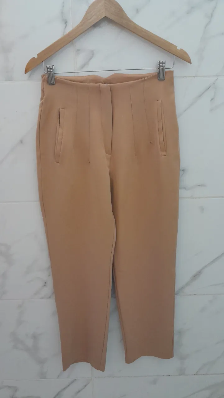 Pantalón color beige, con bolsillos delanteros y cierre.
