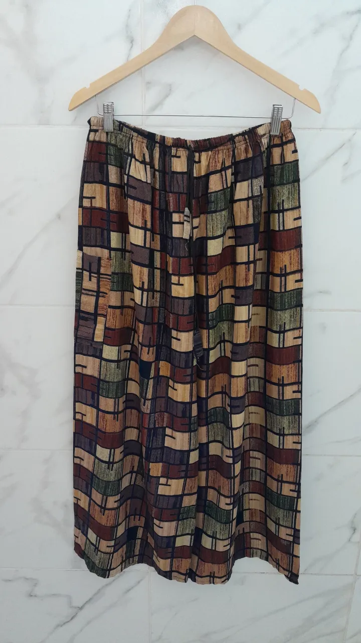Pantalón largo estampado con motivos geométricos en tonos tierra, verde y azul. Posee cintura elastizada con cordón ajustable y bolsillos laterales.