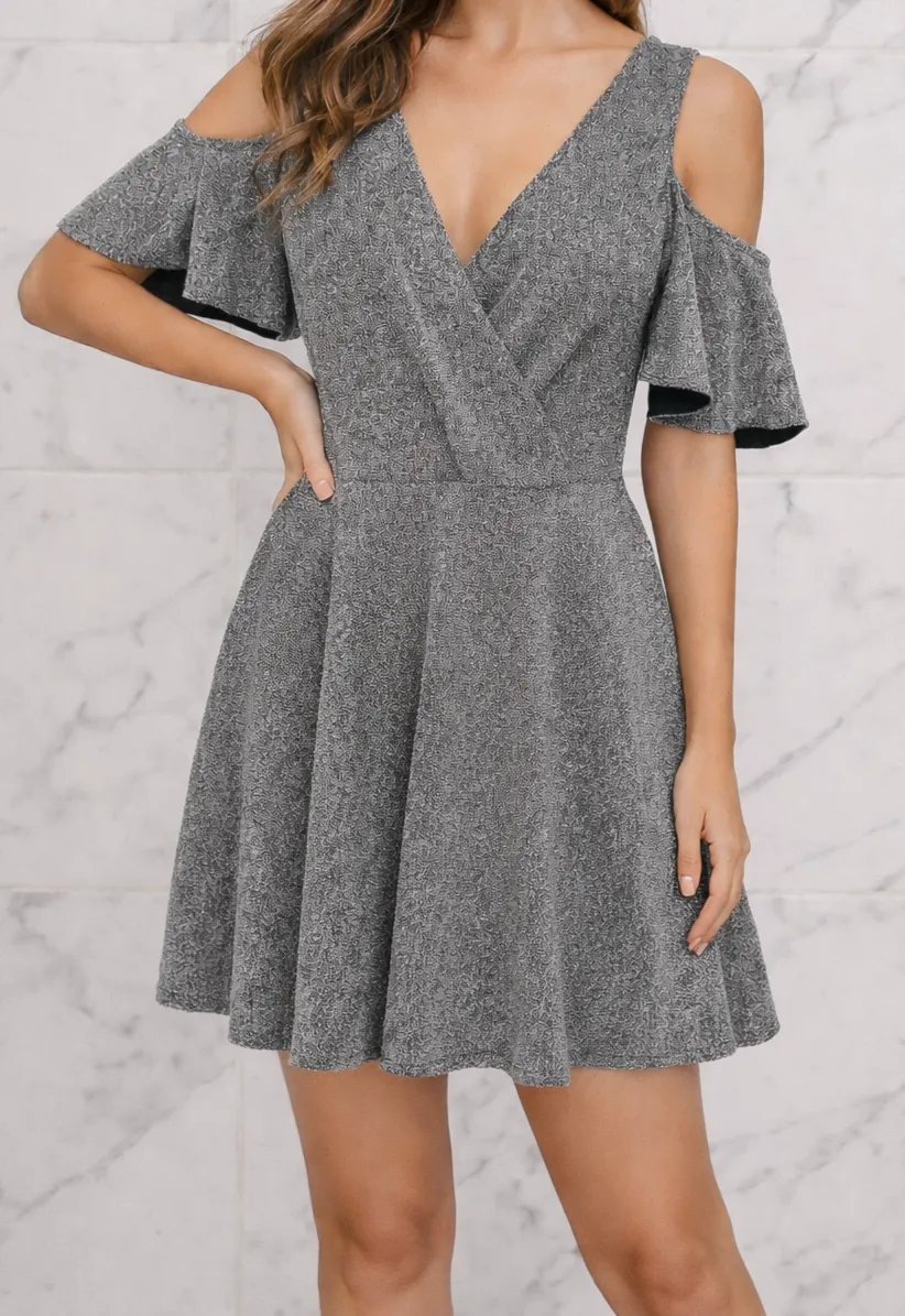 Vestido gris brilloso con escote en V cruzado y mangas cortas con volados. Posee hombros descubiertos.