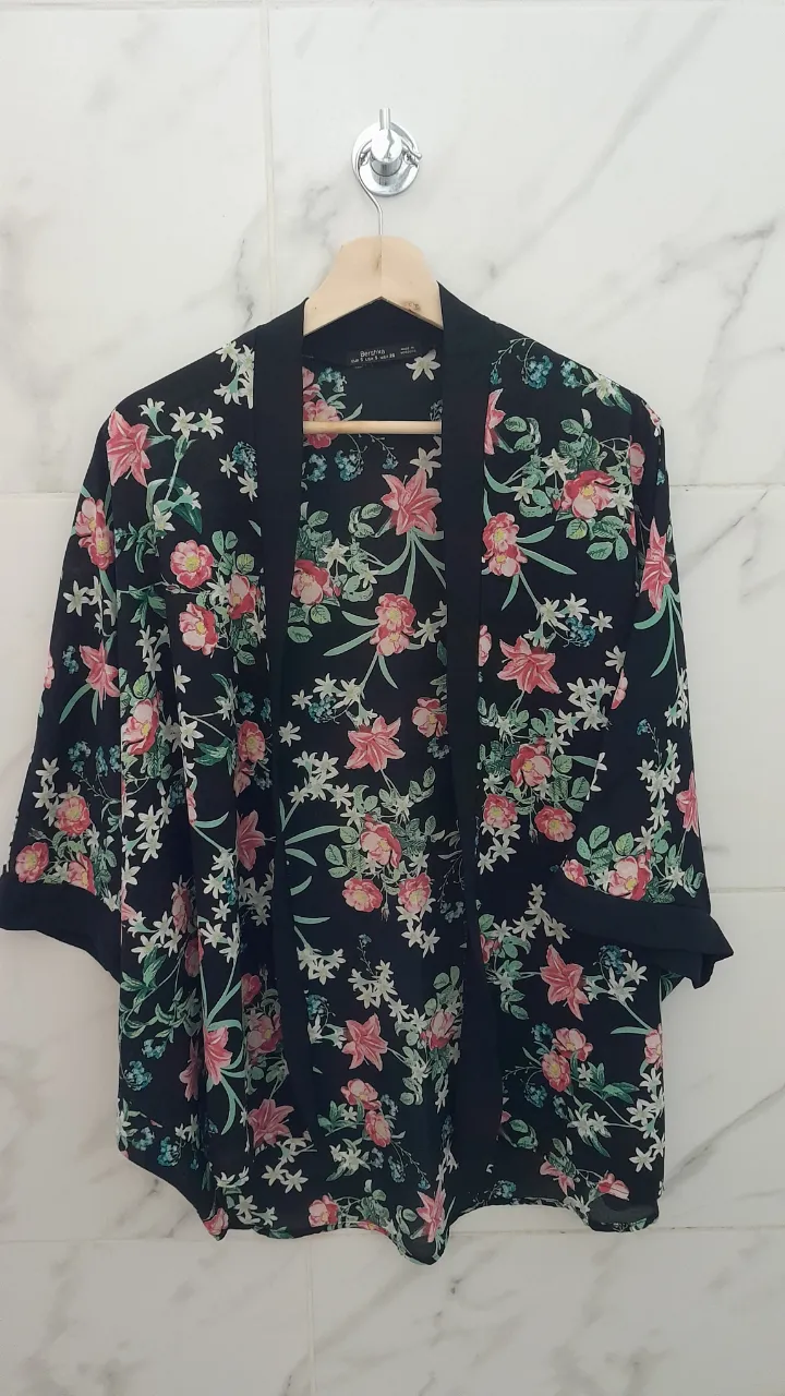 Kimono negro con estampado floral en tonos rosas, blancos y celestes. Posee mangas cortas y solapa.
