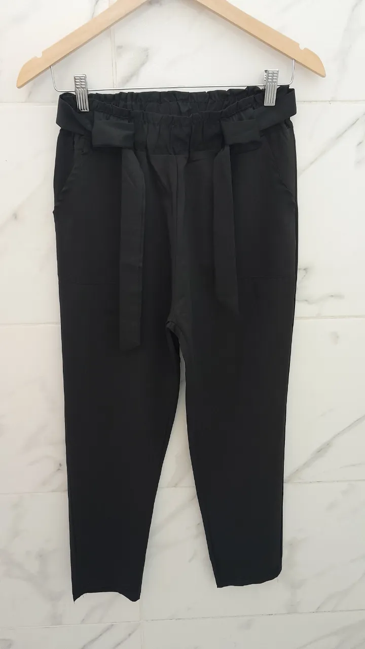 Pantalón negro con lazo en la cintura y cintura elastizada. Tiene bolsillos laterales.
