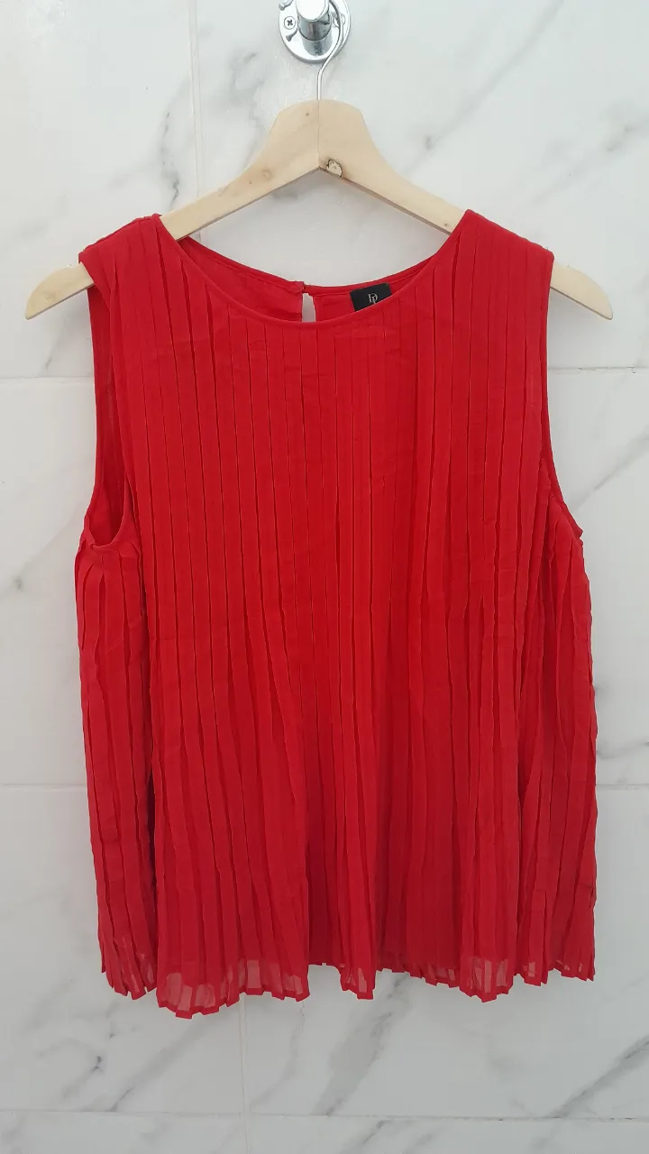 Blusa roja sin mangas con cuello redondo y detalles de plisado vertical en toda la prenda. Posee una abertura en la espalda.