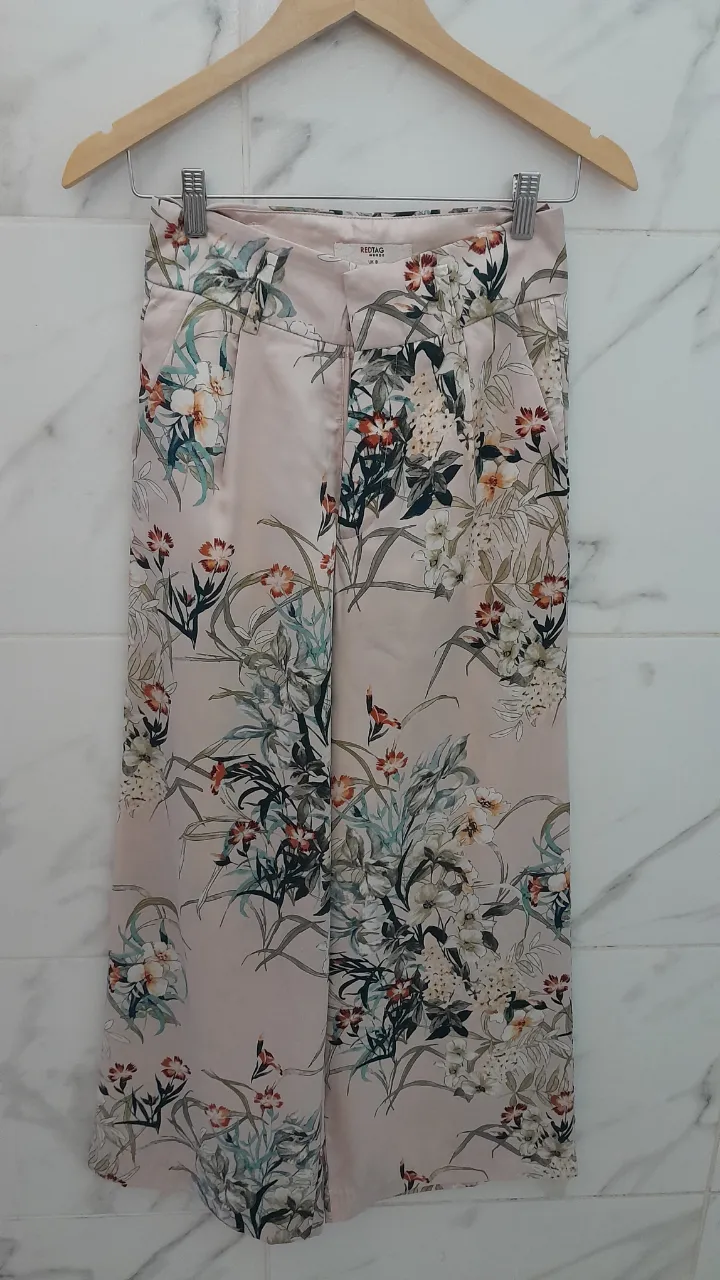 Pantalón de tela con estampado floral en tonos pastel. Posee bolsillos laterales y cierre con ganchos y botón.
