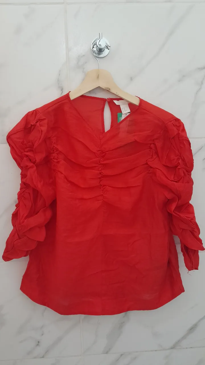 Blusa roja con mangas abullonadas y detalles fruncidos en el frente. Posee un recorte en la espalda.