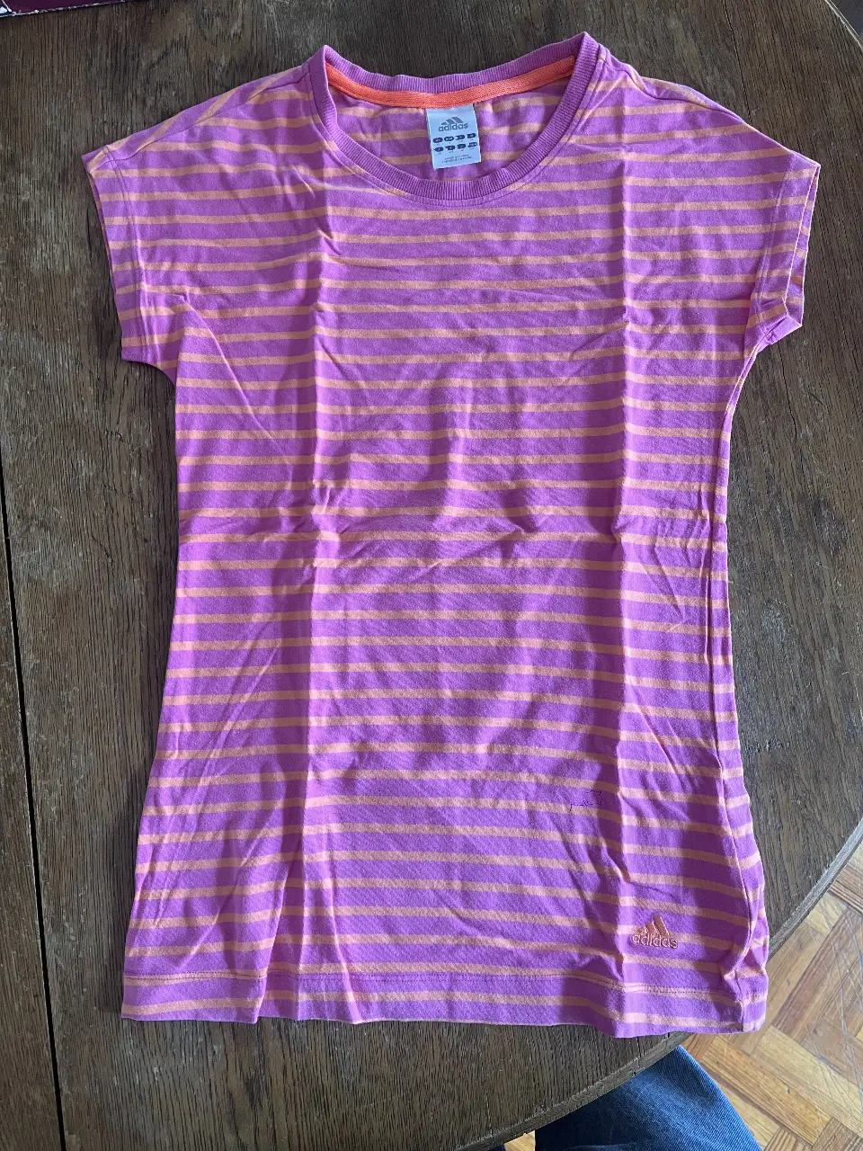 Remera Adidas a rayas horizontales en tonos rosa y naranja. Cuello redondo y manga corta. Ideal para un look casual.