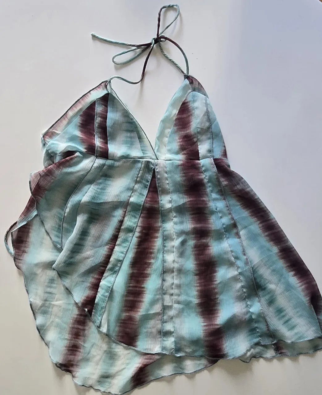 Top sin mangas con escote en V, con tirantes ajustables. Presenta un diseño de rayas en tonos aqua y burdeos. La parte inferior es más amplia, con un corte asimétrico. 