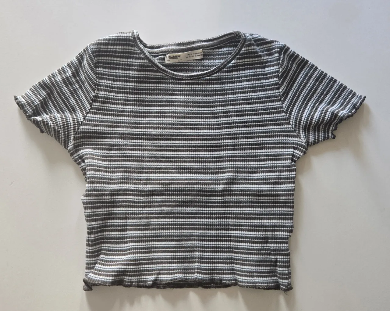 Remera a rayas (verdes y blancas) manga corta con cuello redondo y terminaciones onduladas.