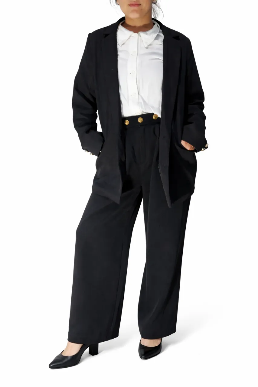 Traje de dos piezas negro, compuesto por un blazer y un pantalón ancho. El blazer tiene botones dorados con diseño de ancla en los puños. El pantalón tiene cintura elastizada y tres botones dorados con diseño de ancla en la parte frontal.