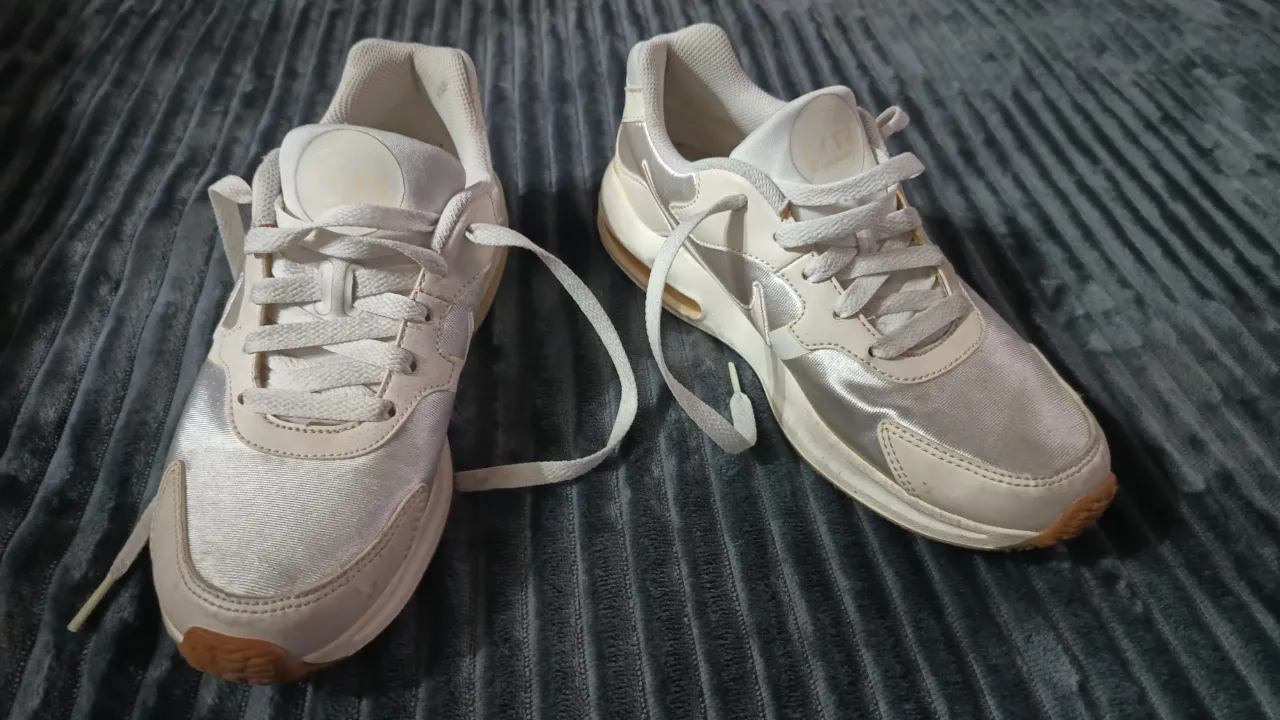 Zapatillas deportivas blancas y plateadas con cordones blancos y suela marrón.